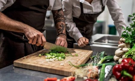 Koch trainiert mit Mitarbeiter das richtige schneiden von Gemüse in der Restaurantküche