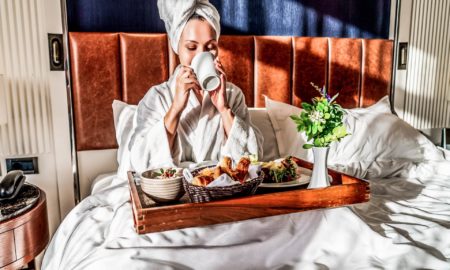 after a restful night a pretty young woman enjoys her breakfast in a hotel bed and drinking coffee