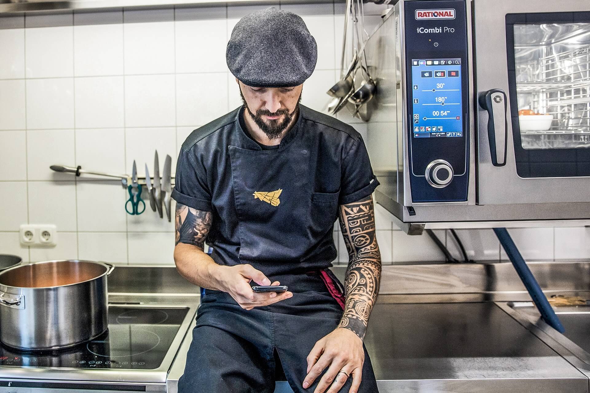 Inked chef sitting in the kitchen checking social media channels for inspirations and information.